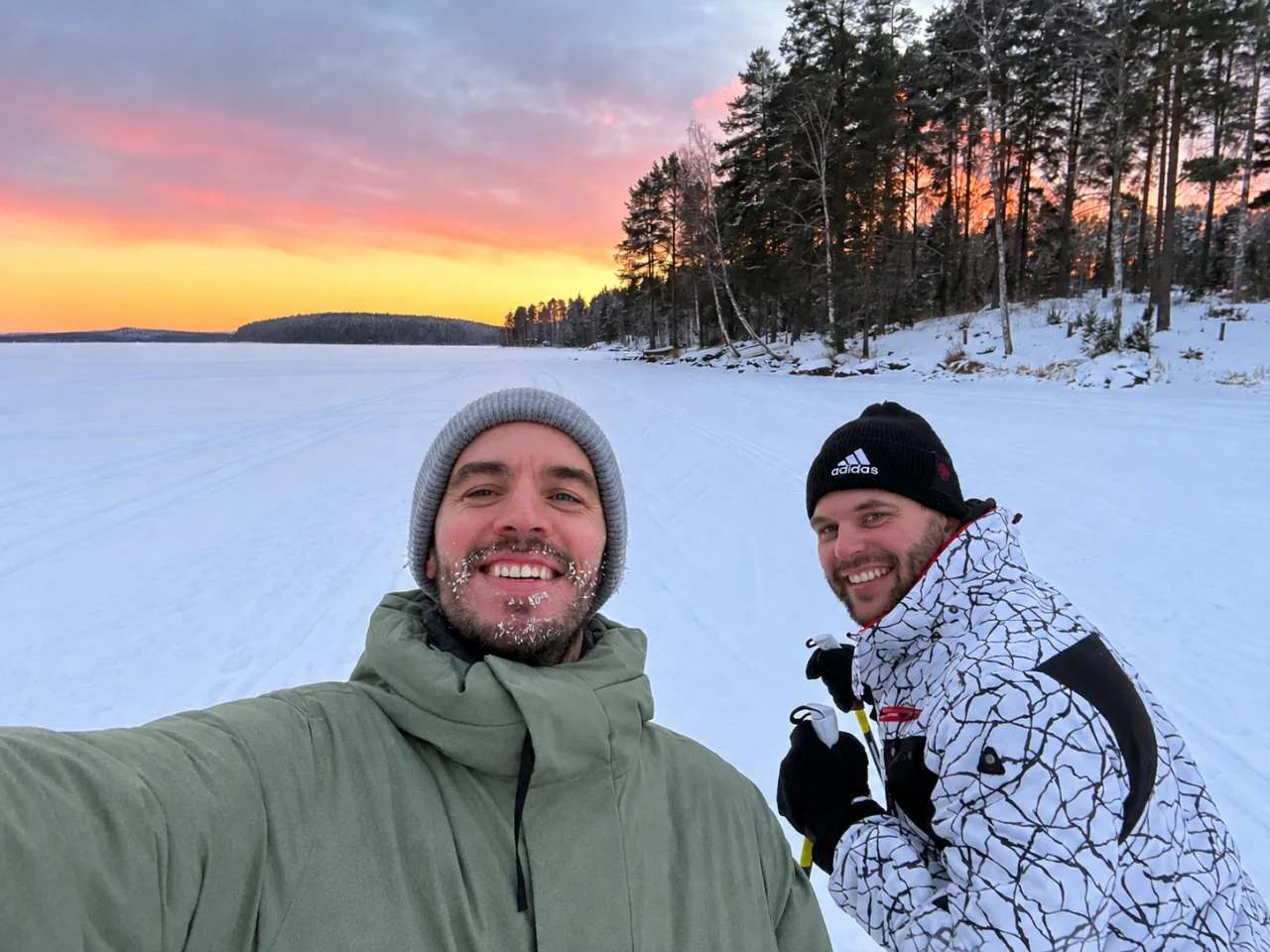 Joey en Lee op een besneeuwd bevroren meer bij zonsondergang, met langlaufstokken in de hand.
