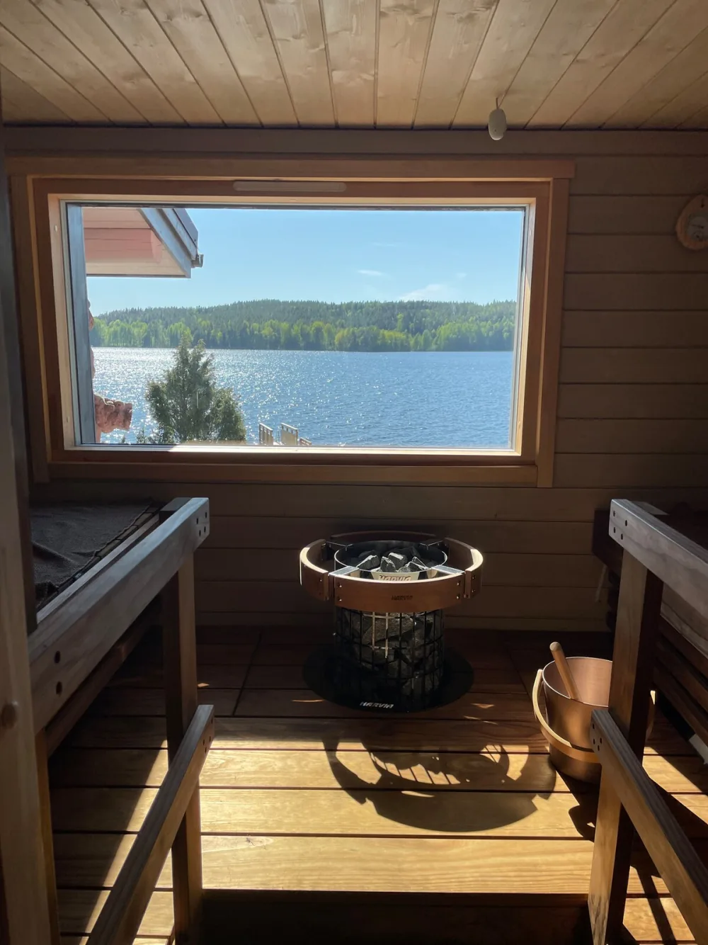 Binnenkant van een sauna met houten banken, een kachel en een raam dat uitkijkt over het meer.